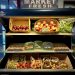Fruit in a cooler on shelves with onions, apples, eggs, sprouts, tomatoes, carrots, garlic and potatoes and a sign above that says Market Fresh