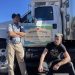 Two men standing next to a refrigerator truck with a sign on the door of the truck that says Amigos Locale, Juice Bar, Coffee, Cafe, Events